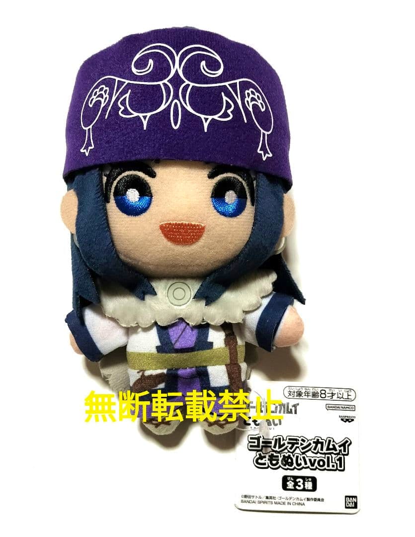 Front-view photo of the Ashirpa plush (ゴールデンカムイ ともぬい) showing the character's purple hat, embroidered face, outfit details, and attached product tag.
