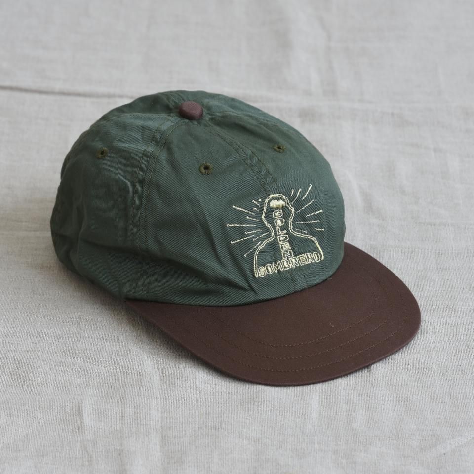 Olive baseball cap with a brown brim displaying the Golden Sombrero logo, shown on a fabric background.
