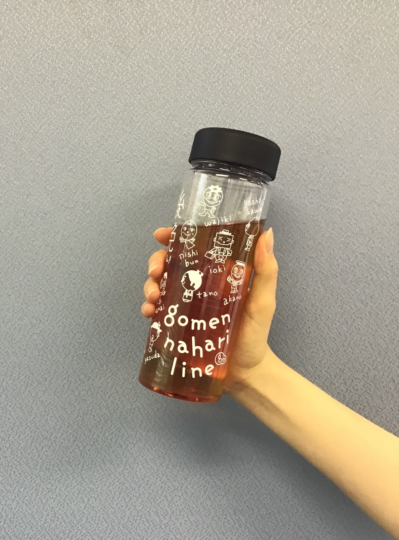 Clear plastic character print bottle with "gomen nahari line" text and a black cap held in a hand against a gray background.
