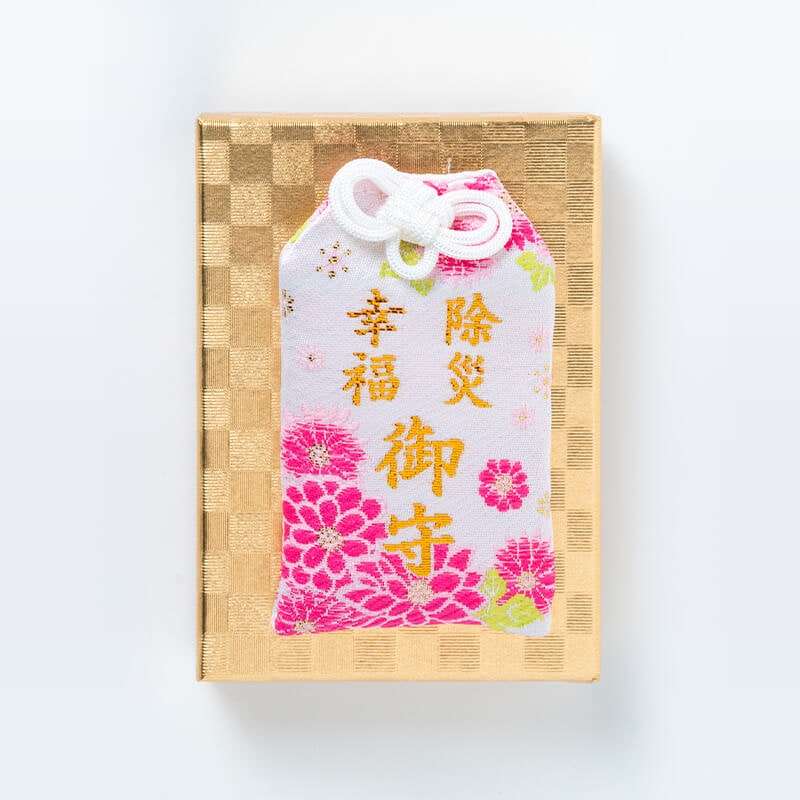 Pink cloth amulet with gold embroidered characters shown on a gold patterned box.