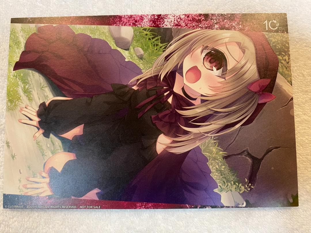 Photo of a postcard showing an anime-style girl in a dark dress lying on grass.