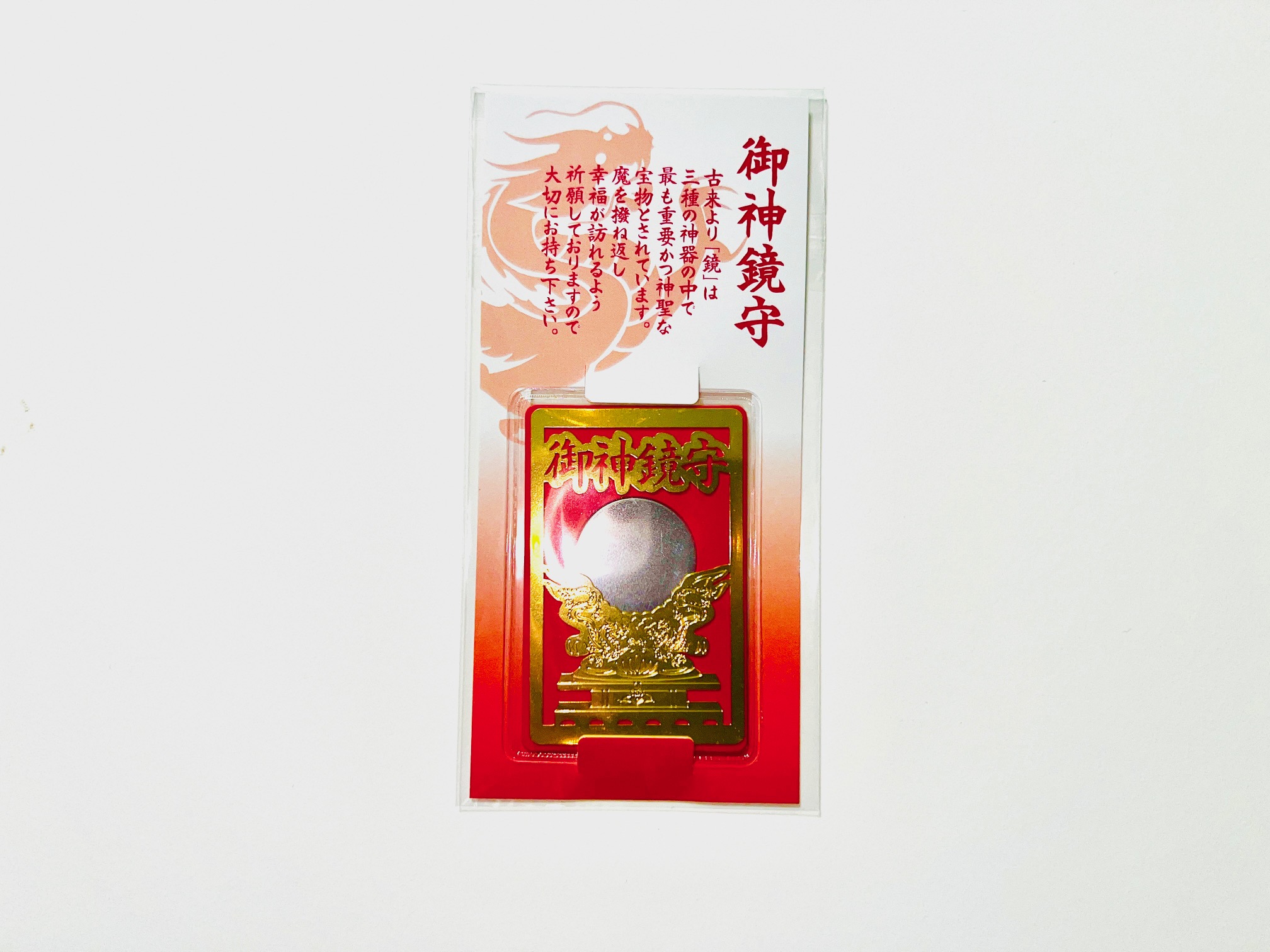 Clear photo of the metal bookmark in its plastic packaging, showing a rectangular red and gold design with a round mirror-like center and Japanese text on the backing.