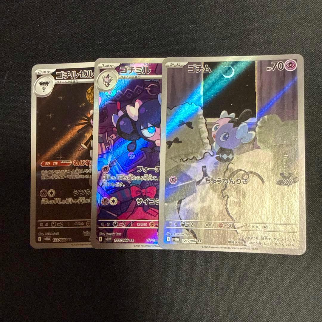 Three holographic trading cards (ゴチム, ゴチミル, ゴチルゼル) arranged overlapping on a dark background.