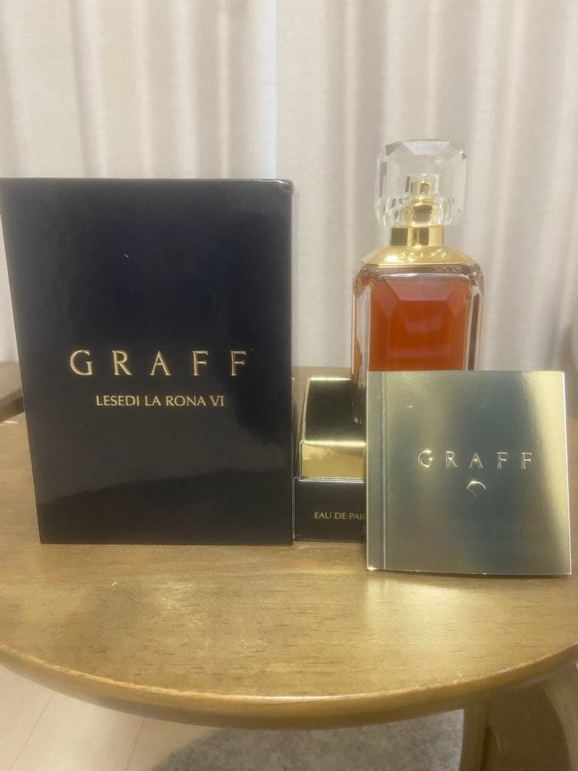GRAFF LESEDI LA RONA VI perfume bottle displayed with its black box and gold lid on a round wooden table.