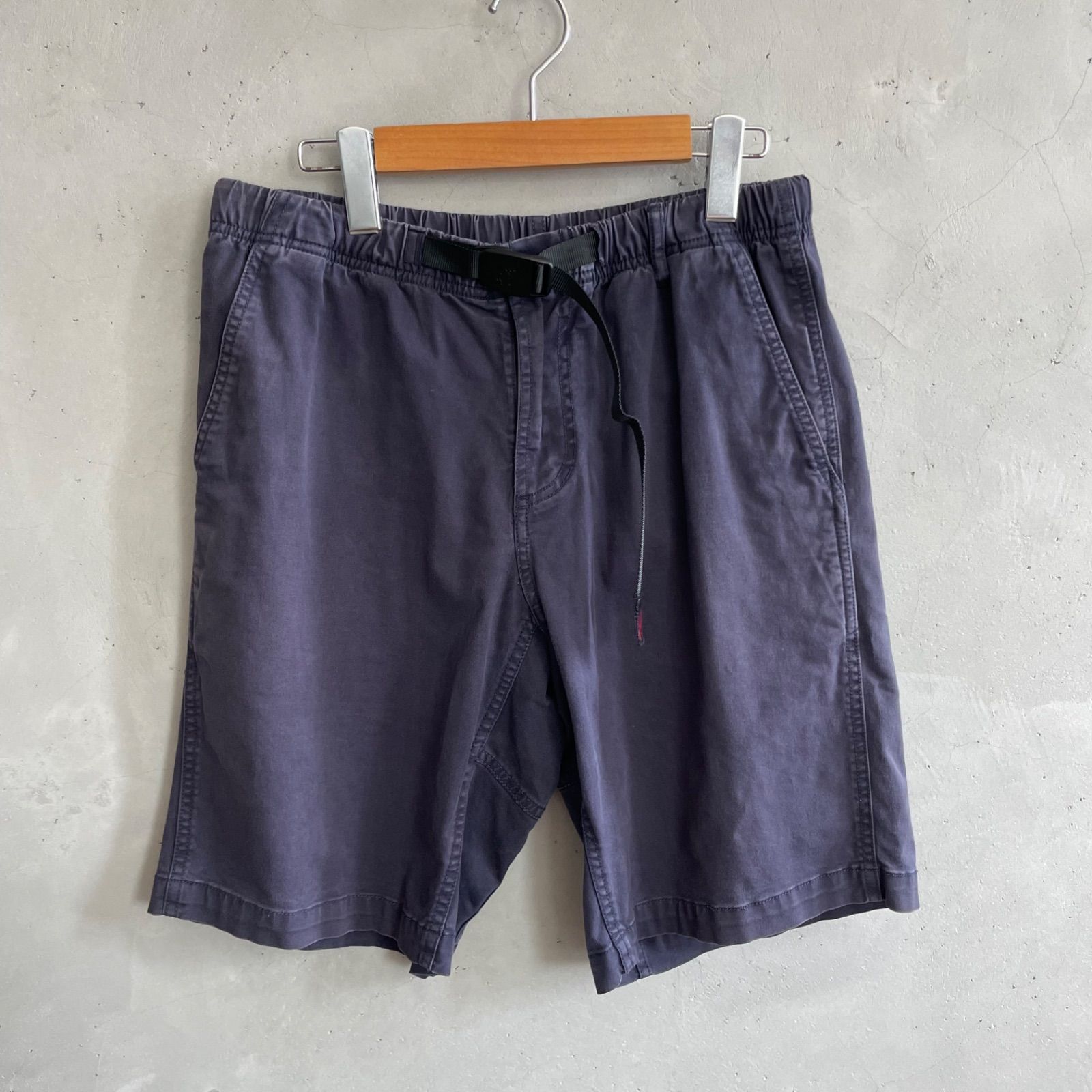 Front view of grey Gramicci men's cotton climbing shorts hanging on a wooden hanger against a concrete wall.
