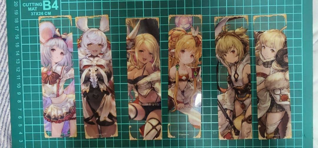 Six rectangular illustrated bookmarks from グラブル 十二神将 laid in a row on a green cutting mat.