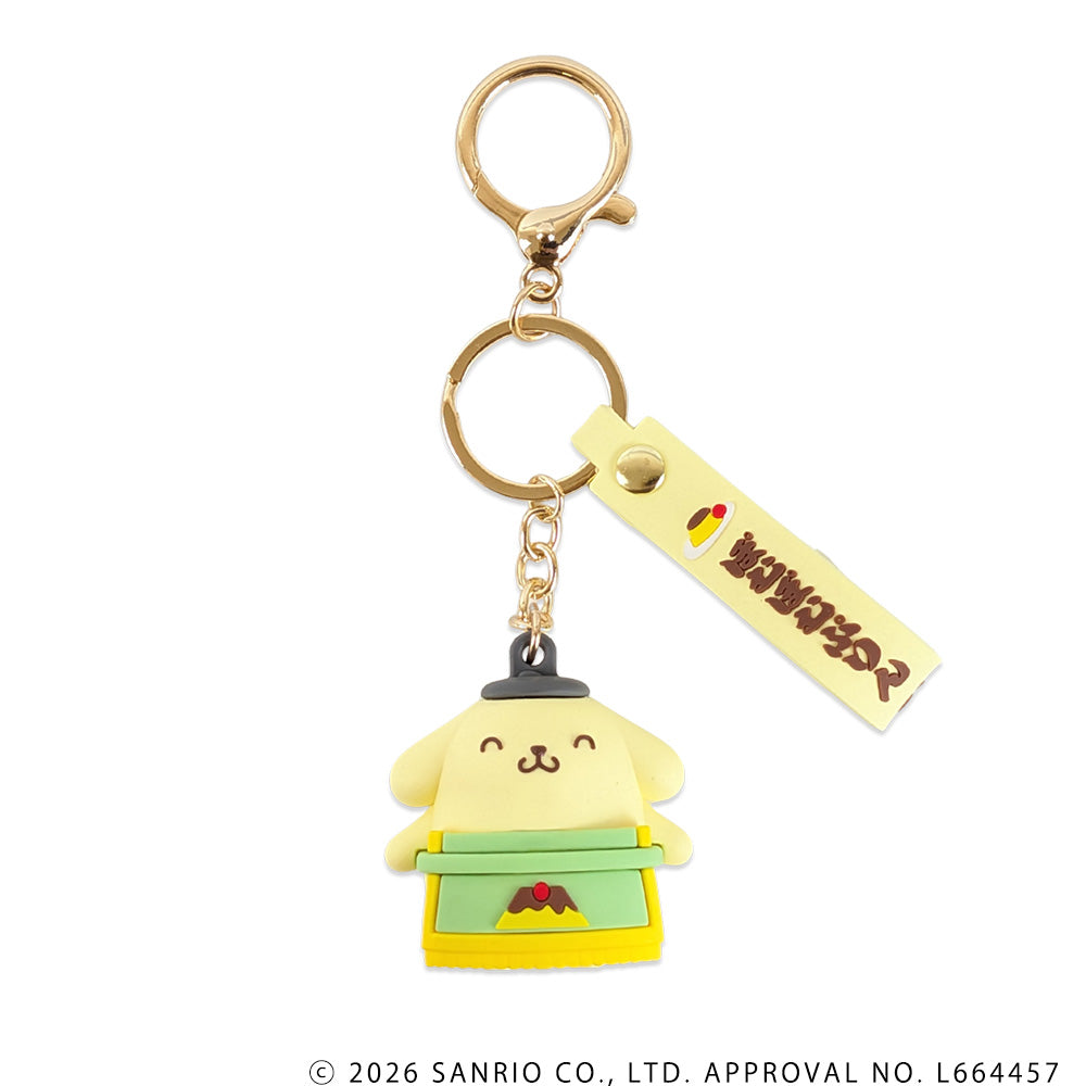 Rubber Pompompurin mascot keychain wearing a green and yellow sumo-style outfit, attached to gold-colored metal rings and a yellow tag.