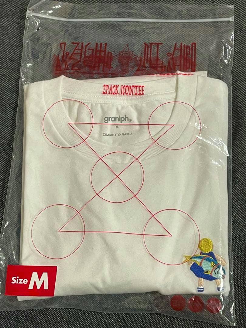 Folded white graniph × 金色のガッシュ T-shirt in clear plastic packaging showing a red geometric print, a small embroidered character, and a Size M label.