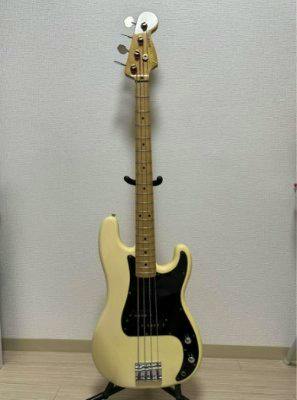 A Greco electric bass guitar standing on a floor stand against a wall, showing the full front of the instrument.