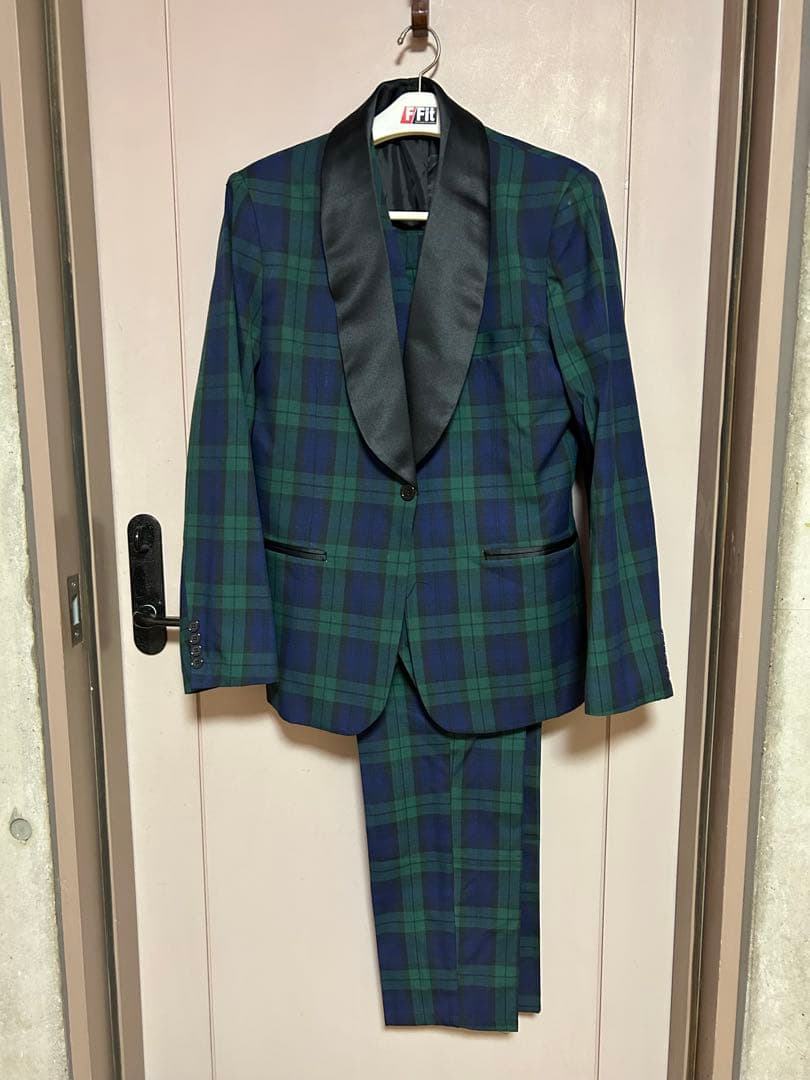 Green and navy check women's tuxedo jacket with black satin lapel and matching trousers hanging on a hanger against a door.