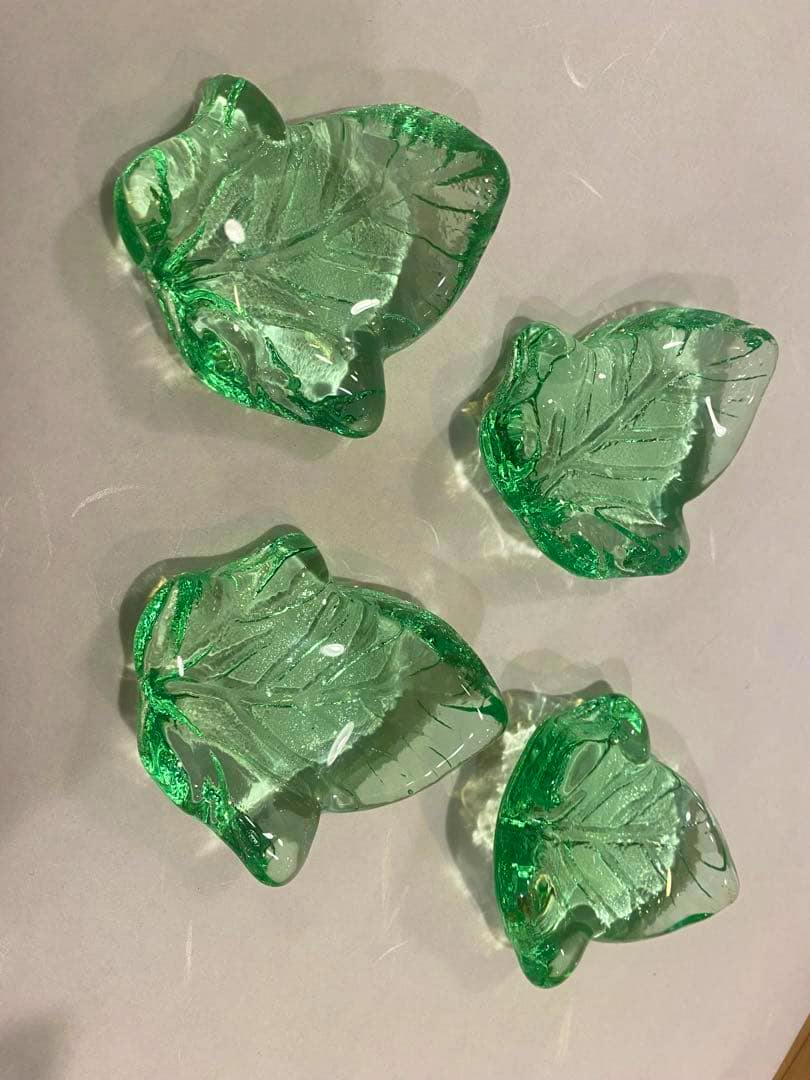 Four green, leaf-shaped glass chopstick rests arranged on a light surface.