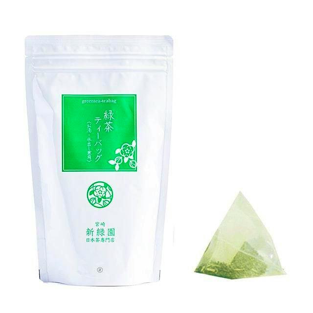 A white resealable pouch of green tea with a green label shown beside a pyramid tea bag.