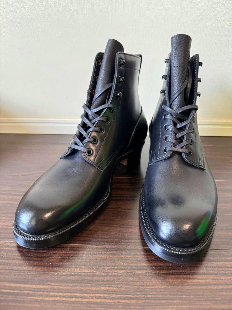 Front-facing view of a pair of black boxcalf leather GRIFFIN boots on a wooden floor.