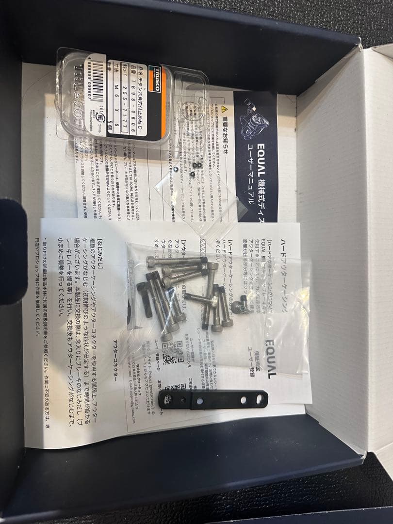 Open box containing a plastic bag of metal bolts, a small metal bracket, and instruction sheets for the GROWTAC EQUAL.