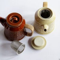 Two porcelain teapots with lids and a metal infuser displayed on a white background.