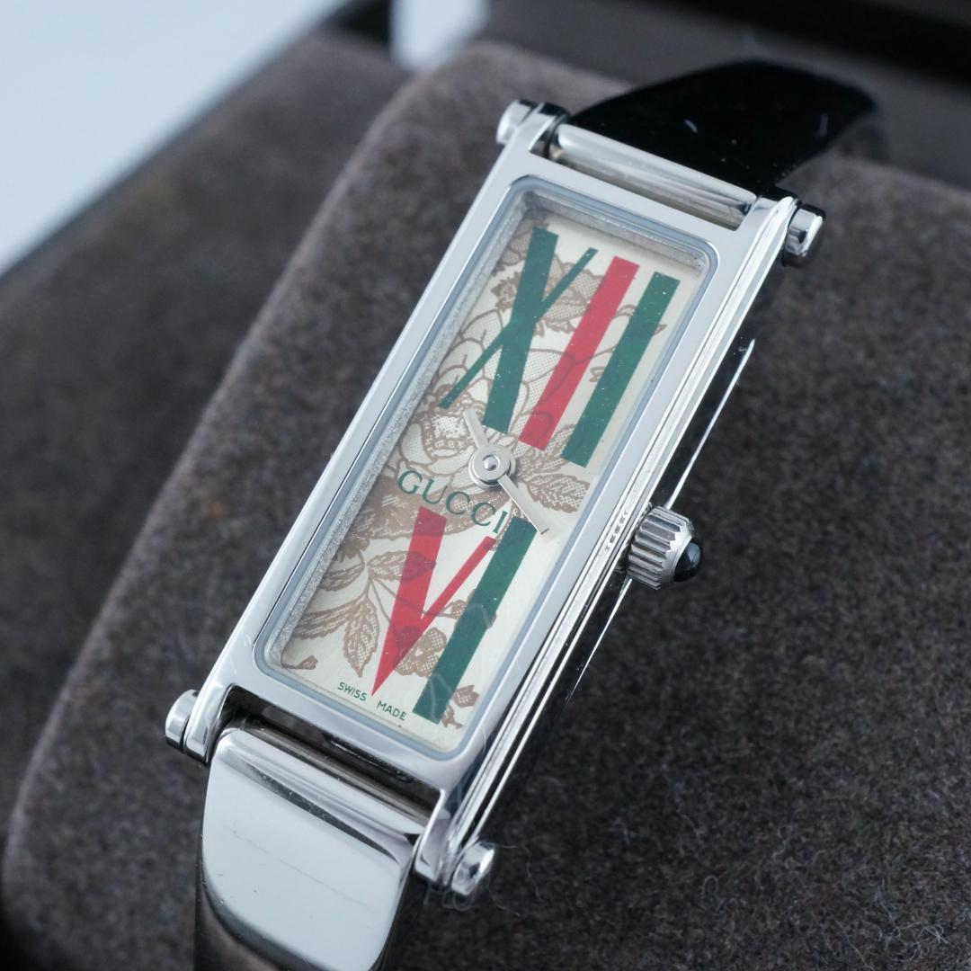 Close-up of a rectangular metal-cased Gucci women's watch showing a floral-patterned dial with red and green stripes.