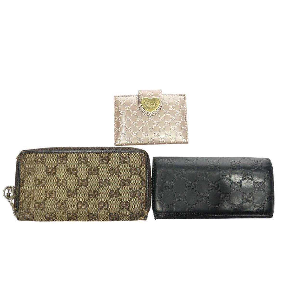 Three GUCCI small wallets and a card case (brown GG canvas zip wallet, black GG-embossed long wallet, and pink card case) shown on a white background.
