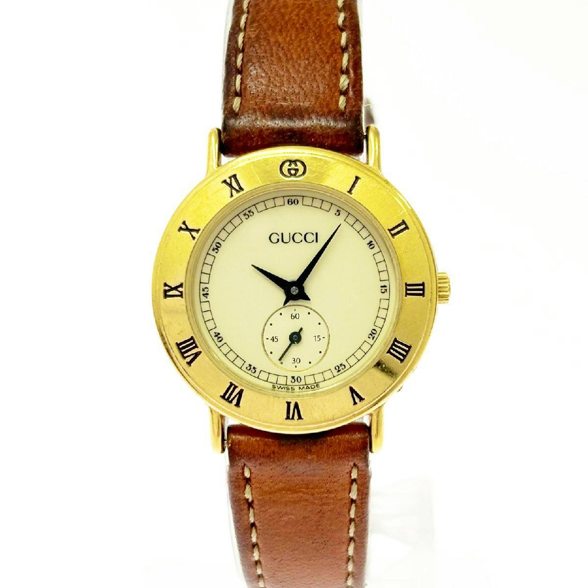 Front view of the GUCCI 3000.2.L round gold-tone quartz wristwatch with cream dial, Roman numerals on the bezel, small seconds subdial, and brown leather strap.