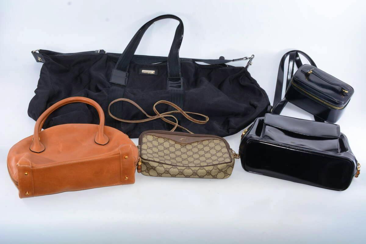 Five GUCCI bags arranged on a white background, including a large black duffel, a brown leather handbag, a beige GG monogram crossbody, a black patent rectangular bag, and a small black zippered pouch.