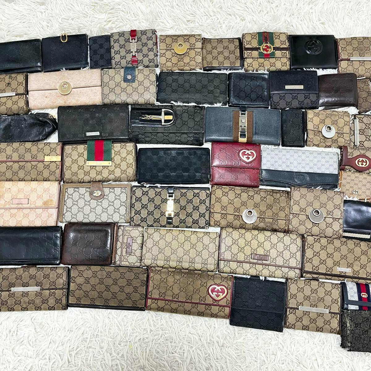 Multiple GUCCI wallets, coin cases, and key cases in canvas and leather arranged on a white textured rug.
