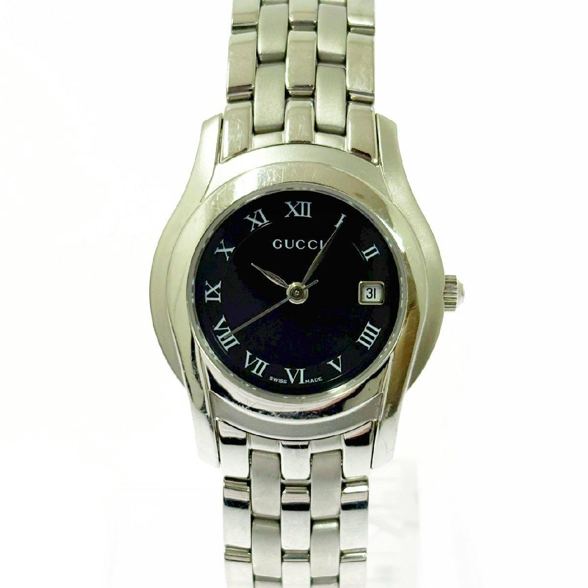 Front view of a GUCCI women's stainless steel wristwatch with a black dial, Roman numerals, date window, and metal link bracelet.