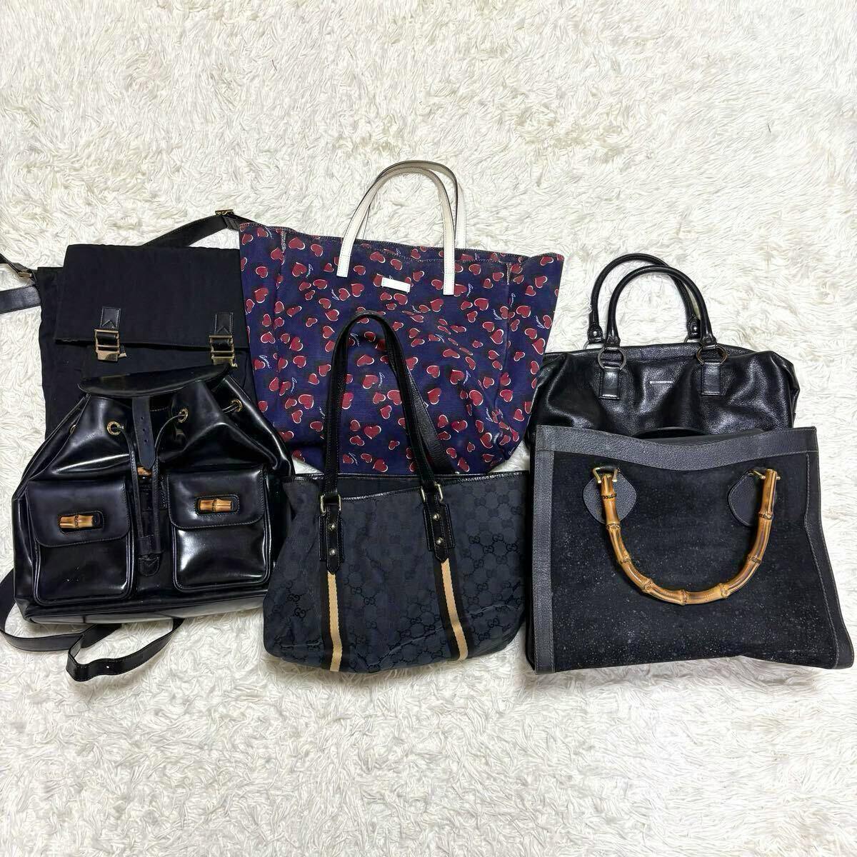 Six Gucci bags (tote, handbag, boston bag, backpack and others) arranged on a white rug showing various GG canvas and leather styles.