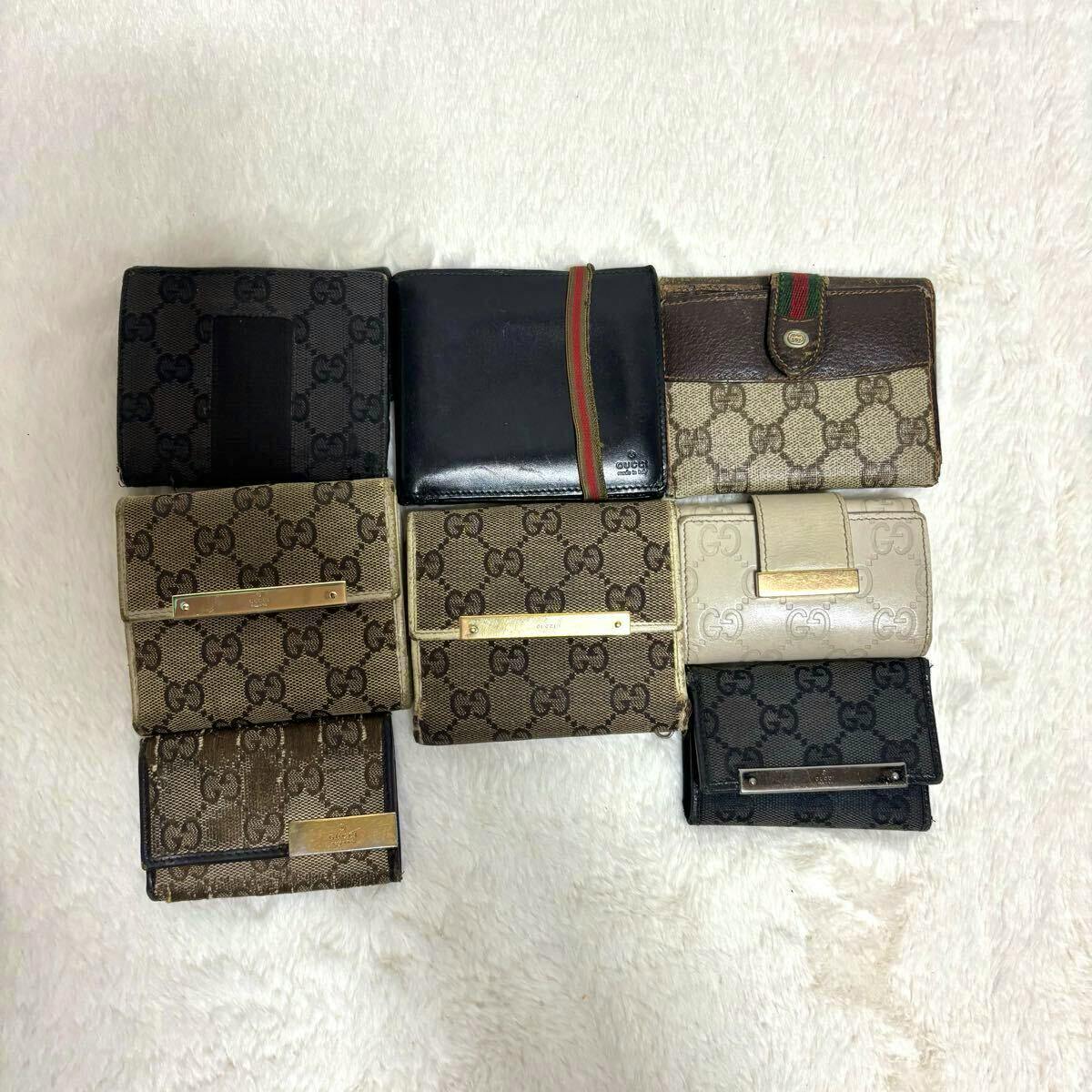 Eight GUCCI wallets and cases in various GG canvas and leather designs arranged on a white surface.