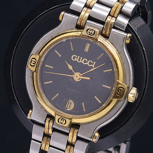 Close-up of a two-tone Gucci ladies' wristwatch showing a black dial with gold-tone bezel and metal bracelet.