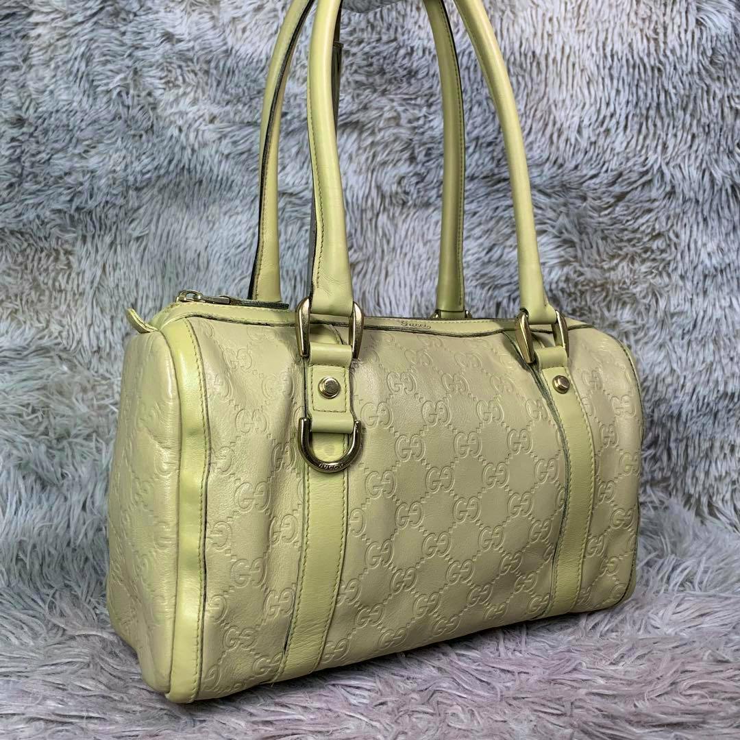 Front-side view of a Gucci mini boston handbag in embossed GG leather with double top handles and gold-tone hardware on a furry background.