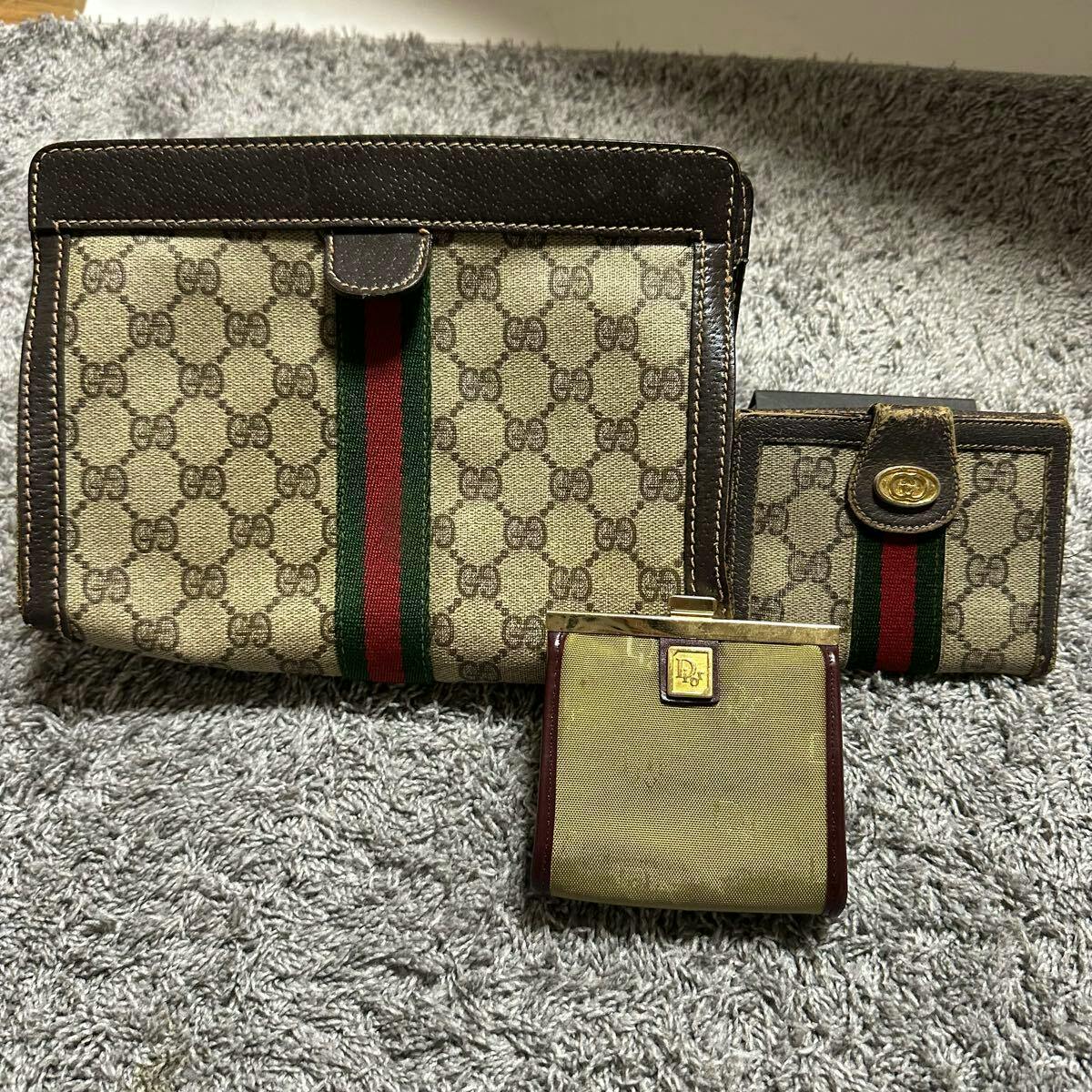 Three wallets and coin purses, two Gucci monogram canvas pieces with green-red stripe and one Dior coin purse, laid on a gray carpet.