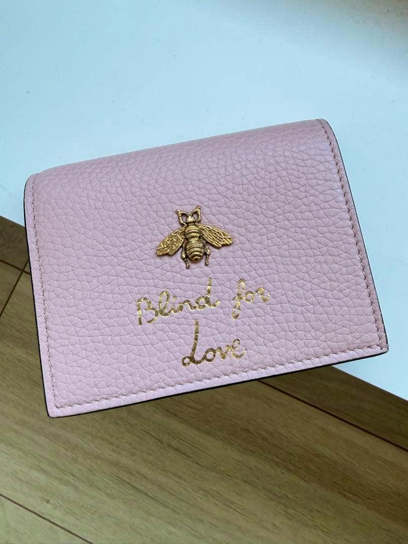 Pink leather bi-fold wallet with a gold bee emblem and gold "Blind for Love" script on the front.