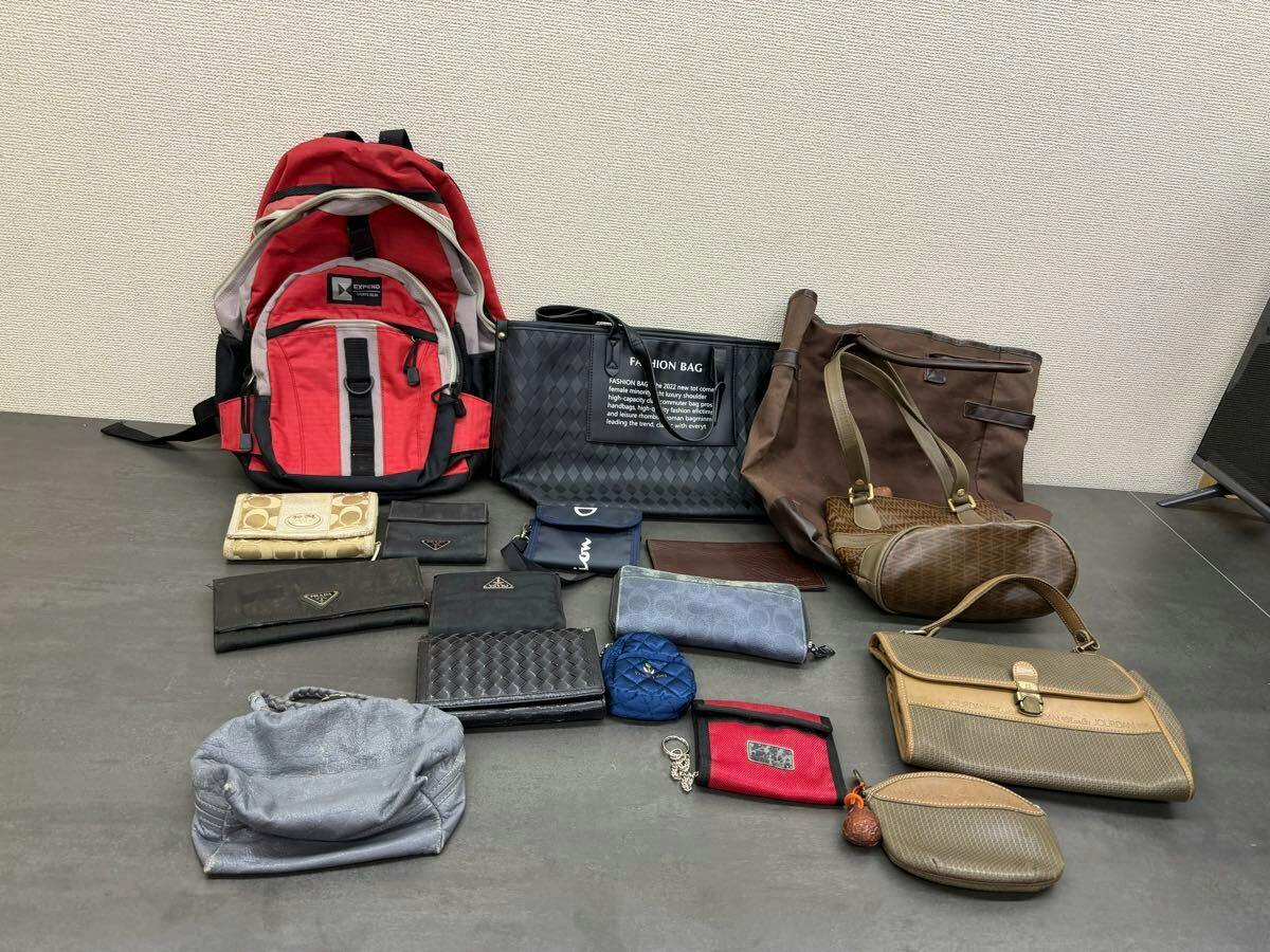 A collection of bags, wallets, and small accessories arranged on a tabletop, including a red backpack, a black tote, brown handbags, and various wallets and pouches.