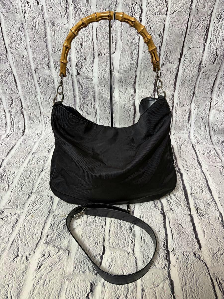Black Gucci canvas 2-way handbag with a bamboo top handle and a detached shoulder strap shown on a textured background.