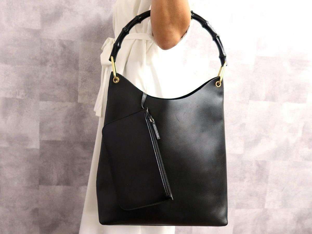 Black GUCCI calf leather bamboo-handle tote bag with gold hardware and an attached pouch, shown being held by a model.