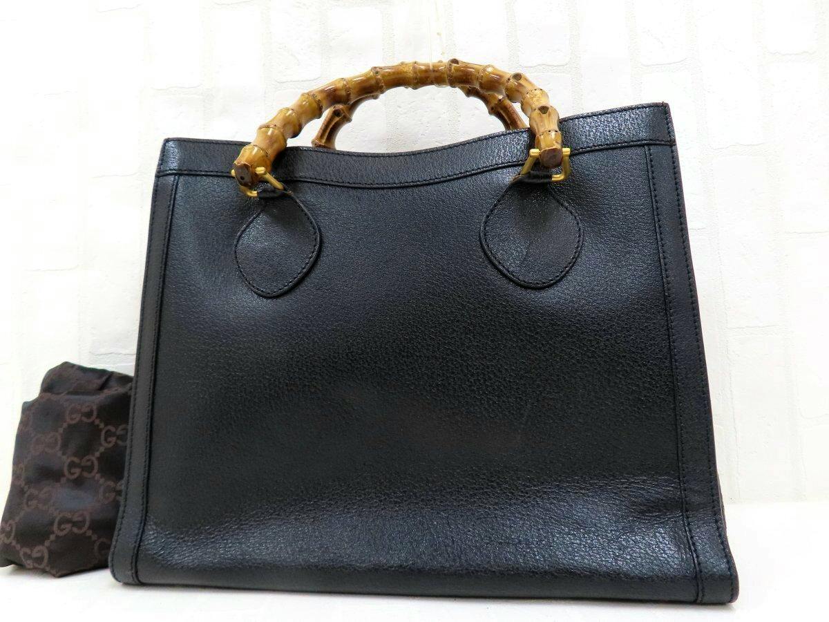 Front view of a black Gucci bamboo-handle calf leather handbag with gold hardware and a Gucci dust bag visible beside it.