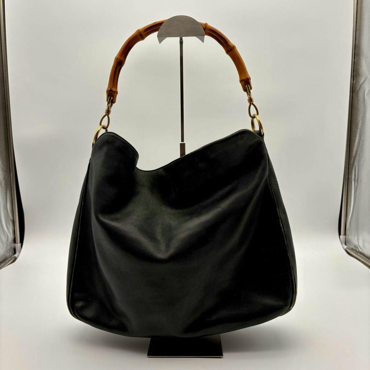 Front view of the black GUCCI bamboo-handle leather one-shoulder tote displayed on a stand against a white background.