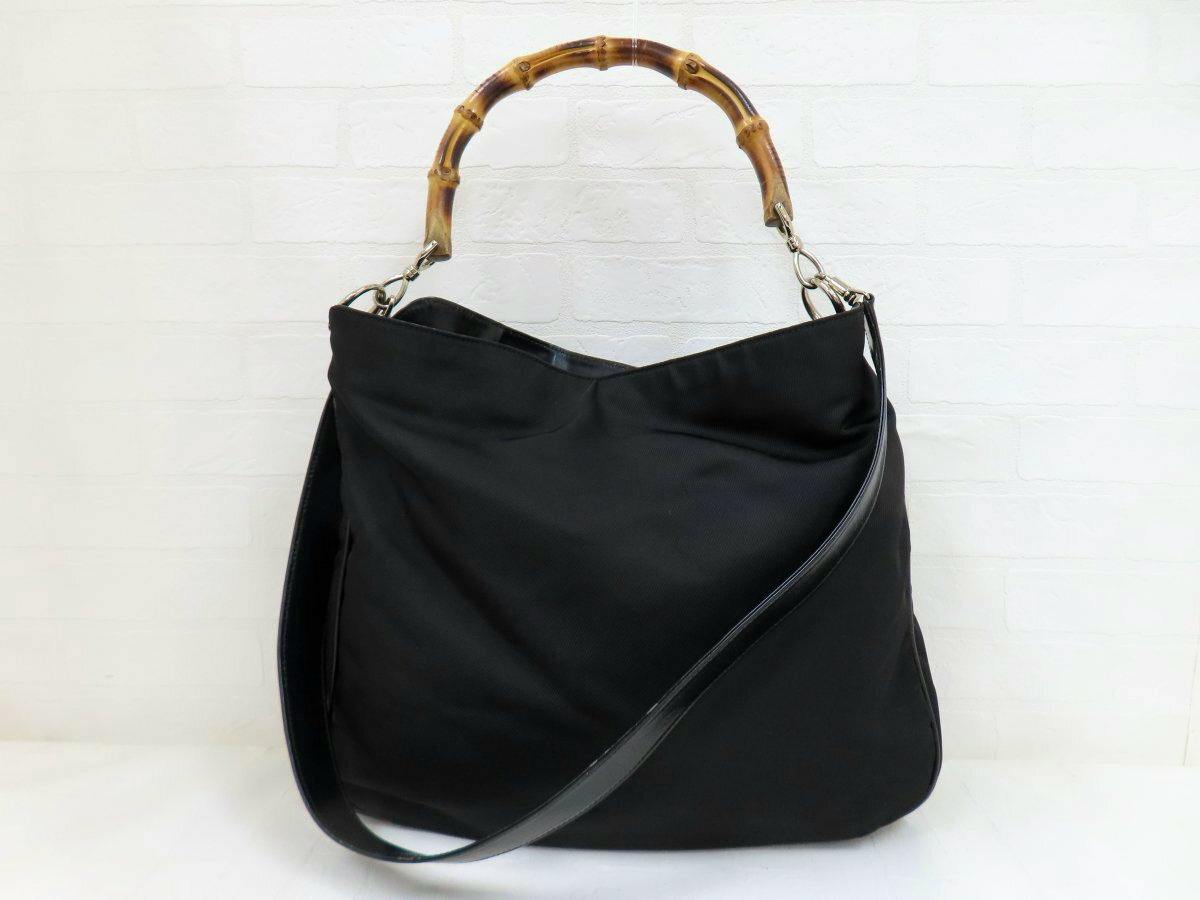 Black Gucci nylon and calf-leather 2way shoulder bag with a bamboo top handle and long shoulder strap photographed against a white background.