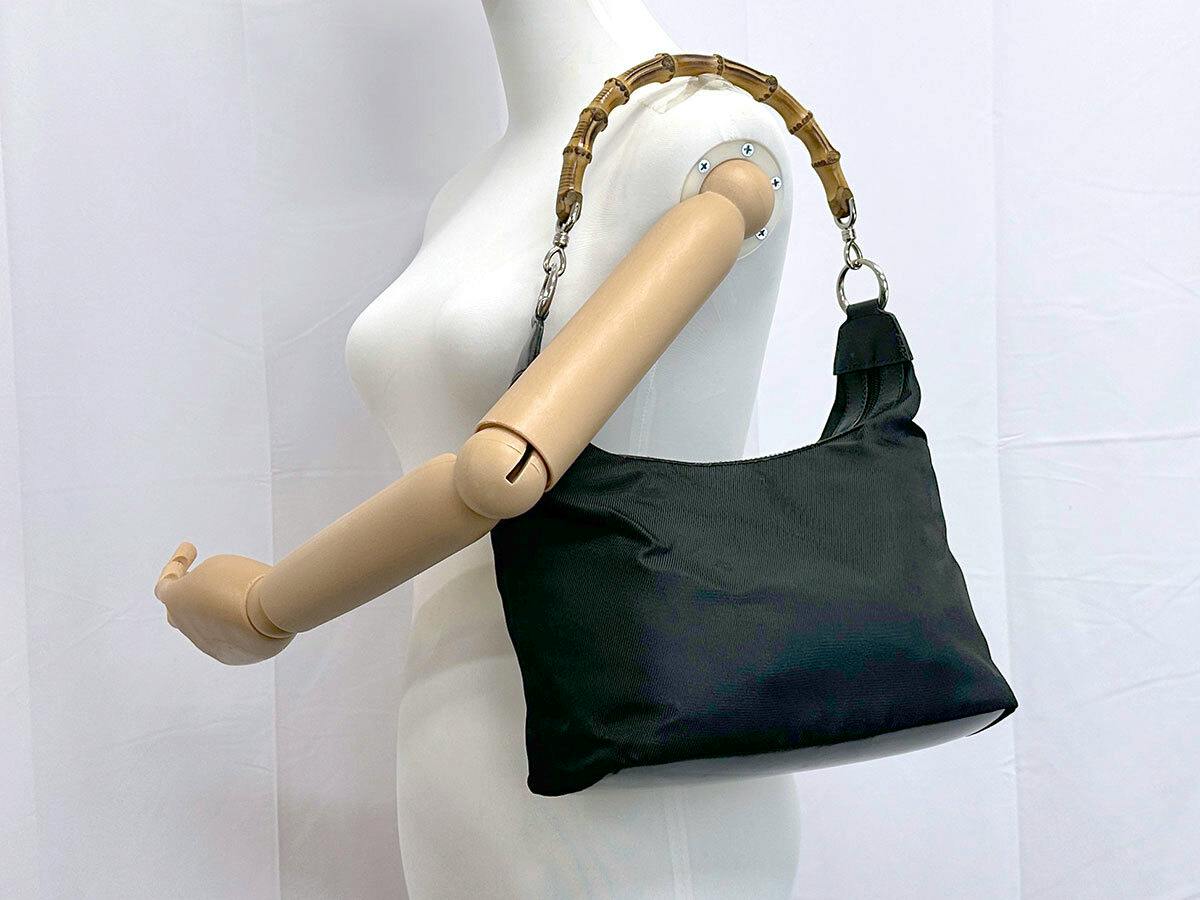 Black Gucci nylon shoulder bag with bamboo handle displayed on a mannequin.