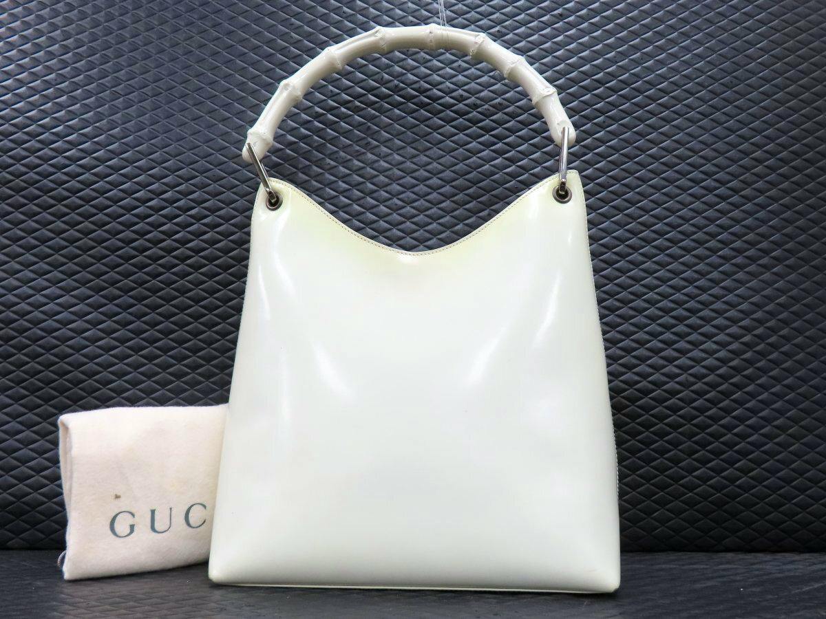 Front view of the white Gucci bamboo-handle patent leather shoulder bag with a small GUCCI dust bag beside it.