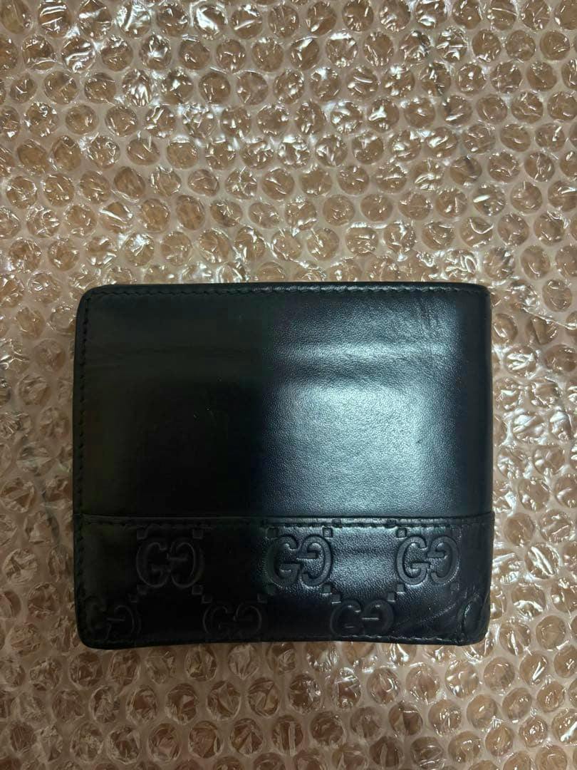Closed black GUCCI bi-fold leather wallet with an embossed GG band, photographed on bubble wrap.