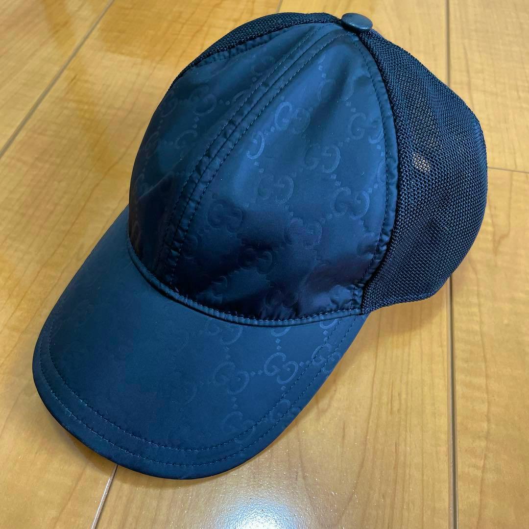 Black Gucci mesh cap showing the front panel and brim placed on a wooden floor.