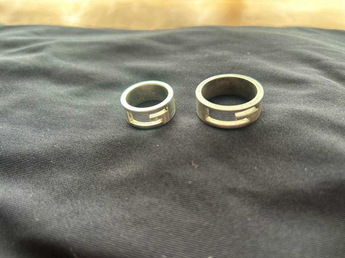 Two silver rings from the GUCCI branded G ring set placed on dark fabric, shown side by side.