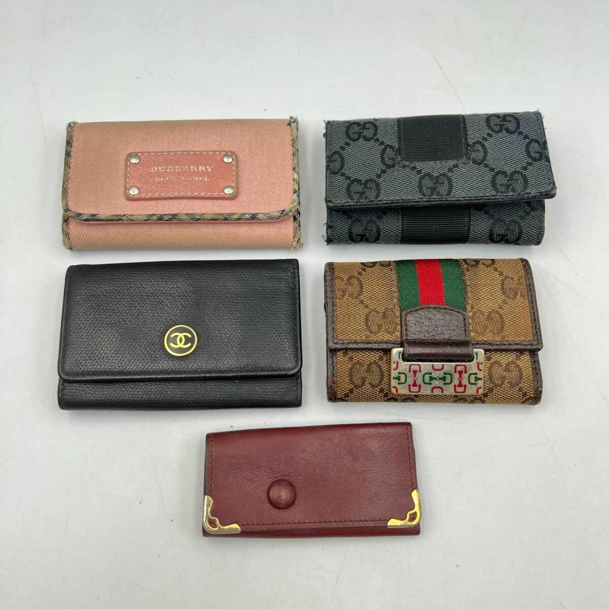 Five key cases and small wallets (Gucci, Burberry, Chanel, Cartier styles) arranged on a white surface.