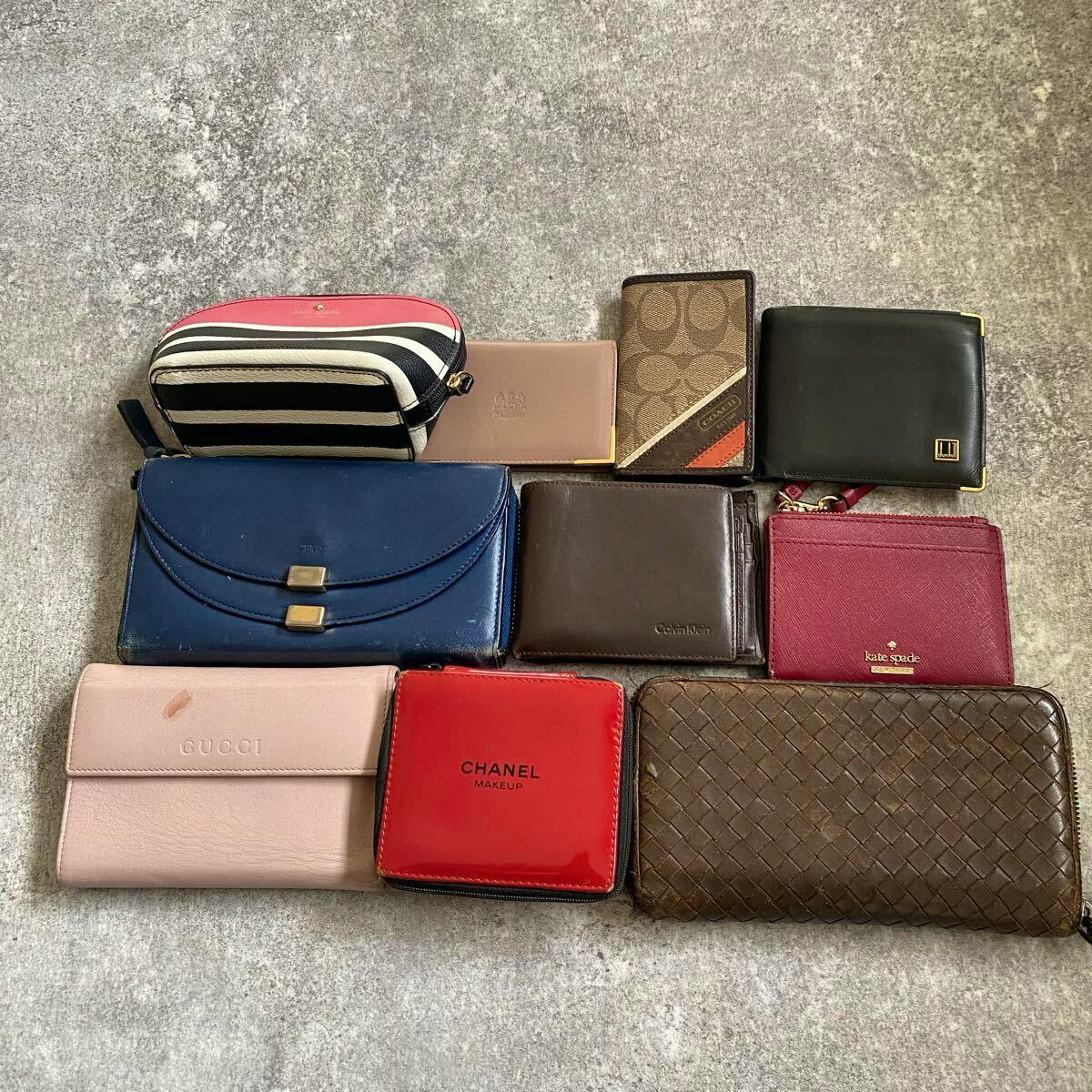 Ten leather wallets and small accessories, including an intrecciato woven leather zip-around wallet, arranged on a gray surface.