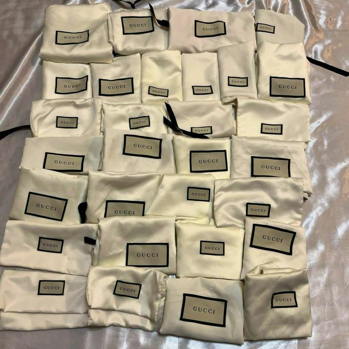 Twenty ivory Gucci cotton storage bags with GUCCI labels arranged on a surface.