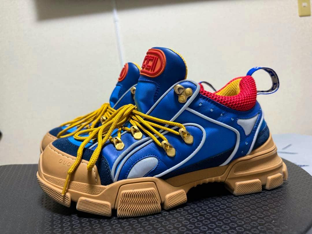 GUCCI Flashtrek men's multicolor sneaker in blue with yellow laces and beige chunky sole photographed on a black textured surface.