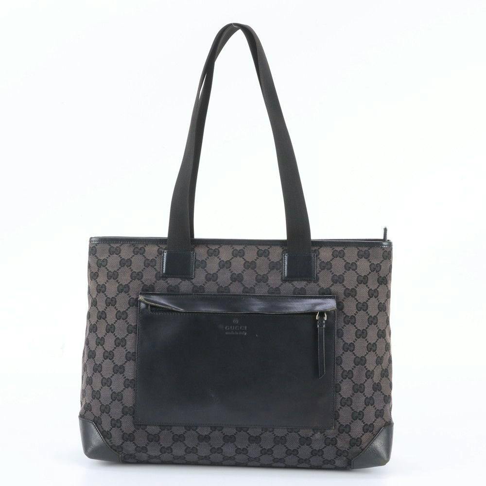 Front view of a black Gucci GG canvas tote bag with a leather front pocket and shoulder straps.