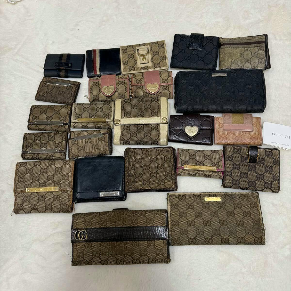 A flat lay of many Gucci wallets and small leather goods in GG canvas and leather arranged on a light background.