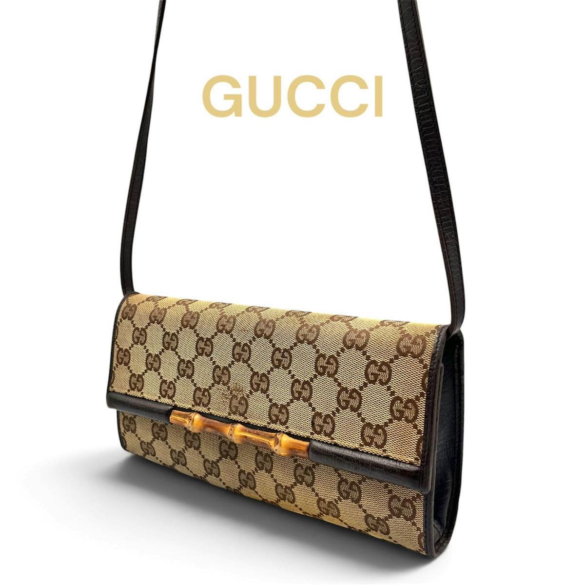 Gucci GG canvas shoulder bag with bamboo front detail and dark leather trim, shown hanging by its strap on a white background.