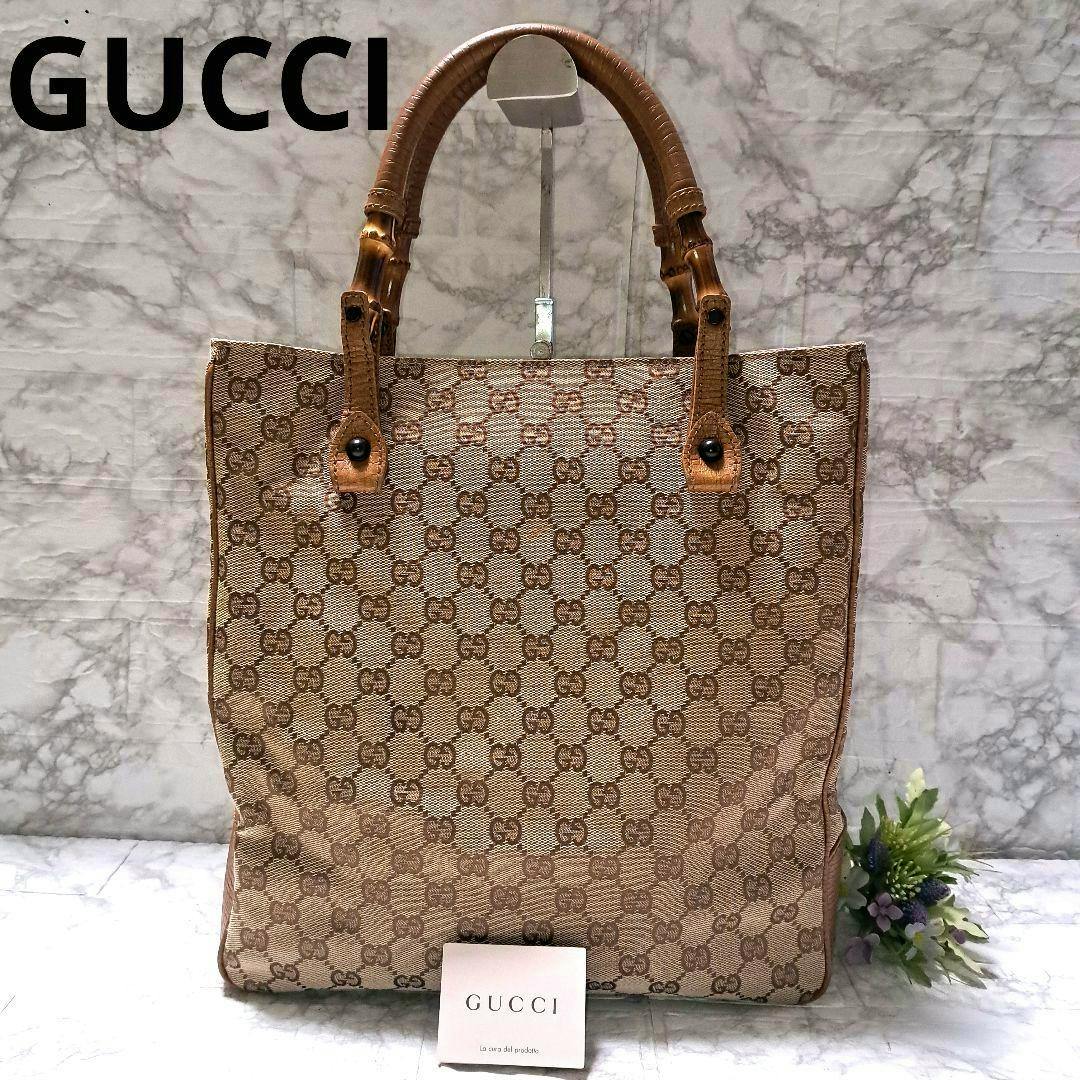 Front view of a Gucci GG canvas tote bag with bamboo-style handles displayed on a stand.
